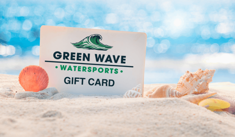 Green Wave Watersports gift card in the sand with shells and a small orange beach ball.
