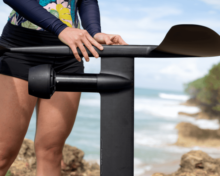 Person holding Lift eFoil mast and wing above ocean rocks, preparing for assembly