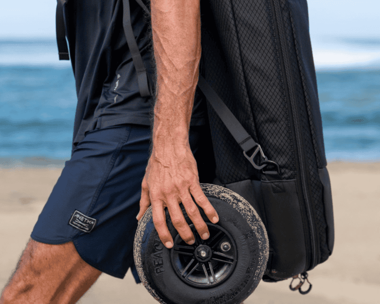Man rolling Lift Foils travel case with rugged wheel on sandy beach