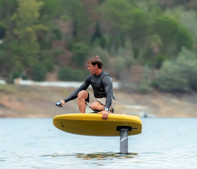 Man crouched on yellow eFoil riding over water holding controller