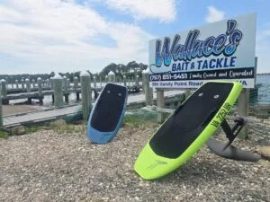 Two eFoil boards in front of Wallace’s Bait & Tackle sign near docks at a marina in Hampton, VA