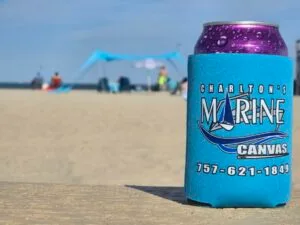 Charlton’s Marine Canvas blue can cooler with logo and phone number on the sand with beach canopy and people in the background