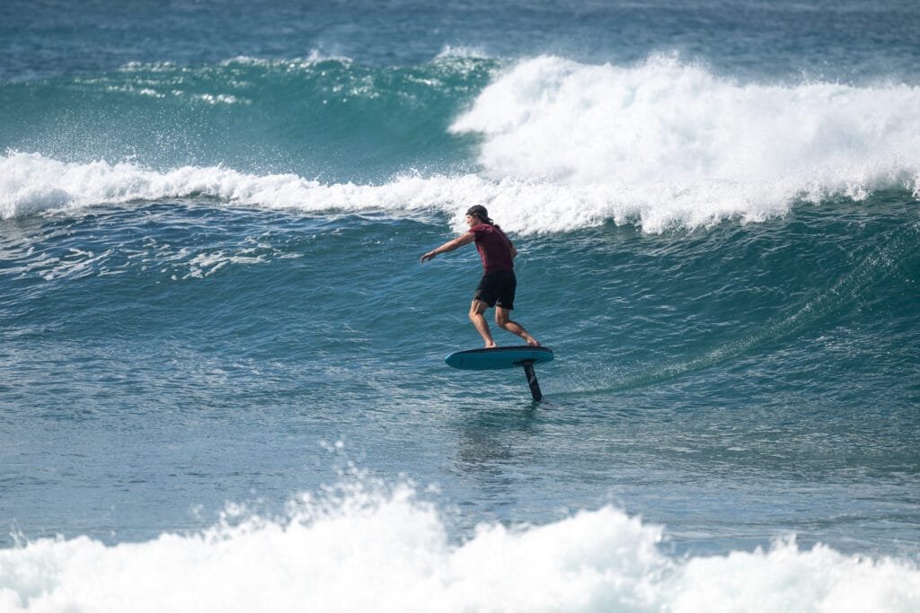 Rider on a LiftX Spark Blue eFoil gliding above ocean waves, wearing a red shirt and black shorts.