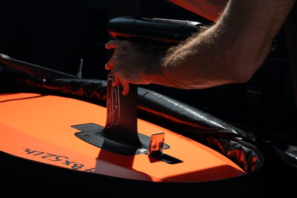 Close-up of hands securing the mast onto the orange LiftX Dawn Patrol eFoil board during assembly.