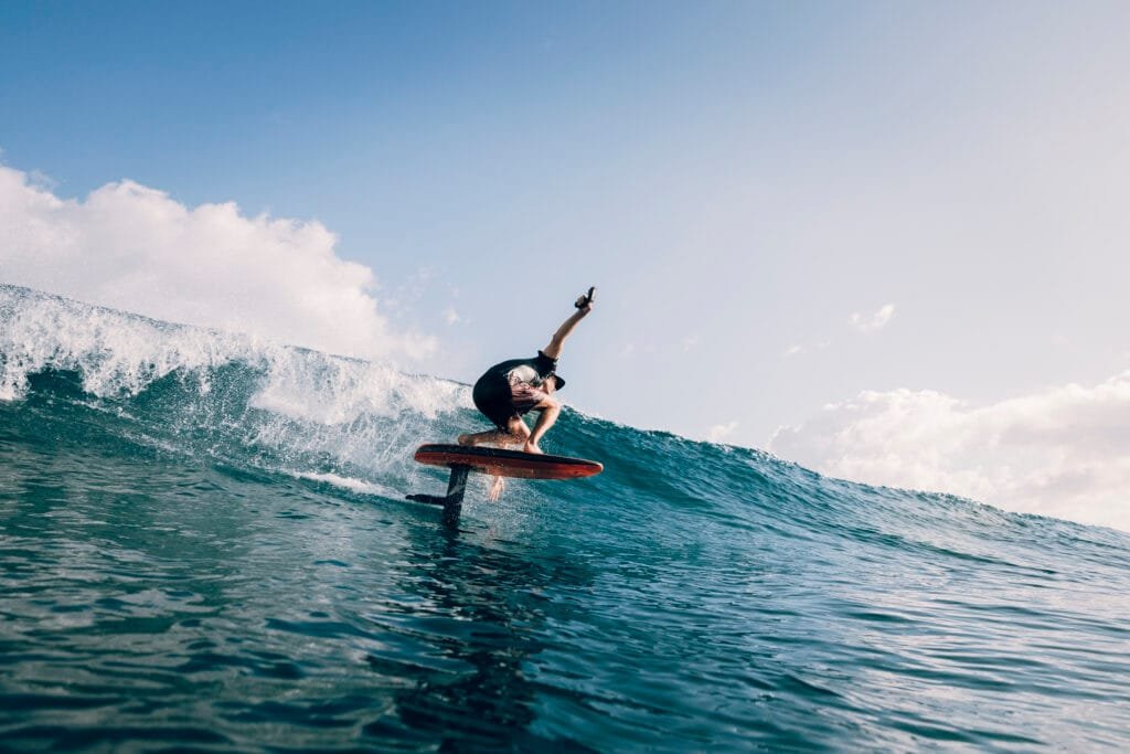 Rider carving across an ocean wave on a bright orange LiftX Dawn Patrol eFoil.