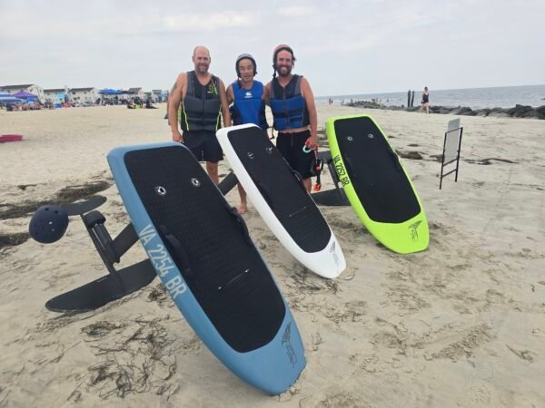Patrick, Jason, and Phi posing beside multiple Lift eFoil boards on Buckroe Beach in Hampton, Virginia.