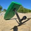 Side-angle view of a custom green electric hydrofoil eFoil board with carbon fiber mast and foil wings on the sand near the Chesapeake Bay in Hampton, Virginia.