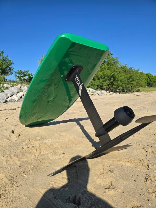 Side-angle view of a custom green electric hydrofoil eFoil board with carbon fiber mast and foil wings on the sand near the Chesapeake Bay in Hampton, Virginia.