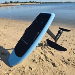 Custom light blue electric hydrofoil eFoil board with black deck pad and foil wings on the sandy shoreline near calm Chesapeake Bay water in Hampton, Virginia.
