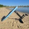 Side view of a custom light blue electric hydrofoil eFoil board with carbon fiber mast and foil wings on a calm beach shoreline in Hampton, Virginia.