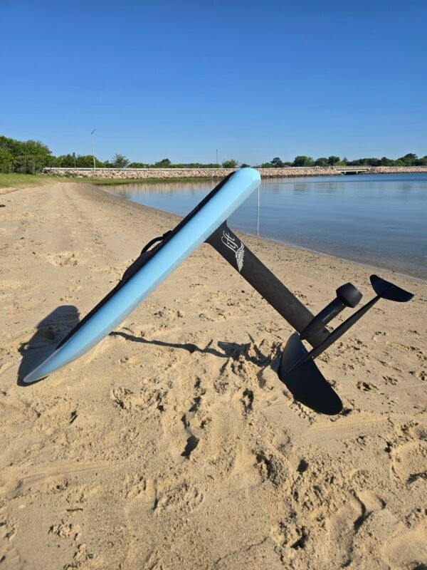 Side view of a custom light blue electric hydrofoil eFoil board with carbon fiber mast and foil wings on a calm beach shoreline in Hampton, Virginia.