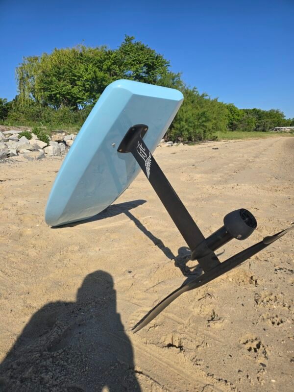 Side view of a custom light blue electric hydrofoil eFoil board with black foil mast and wings on the sand at Buckroe Beach in Hampton, Virginia.