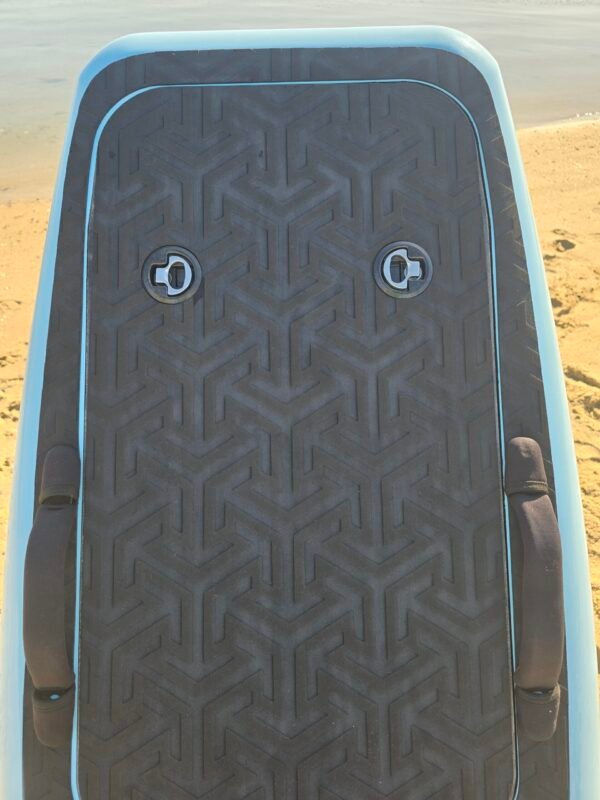 Close-up of a custom light blue eFoil board deck with black traction pad, hatch latches, and carry handles on the beach at Buckroe Beach in Hampton, Virginia.